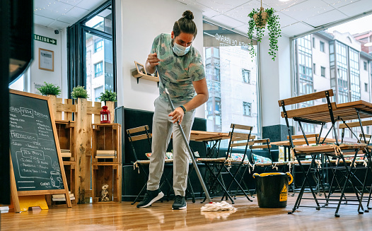 Worker with mask mopping the floor of a restaurant